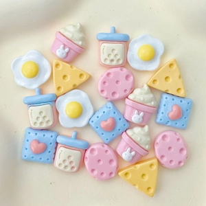 Flat lay of miniature resin DIY food charms including eggs, cheese, and milk tea cups
