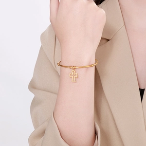 Close-up of a minimalist gold cross charm bangle bracelet on a female wrist