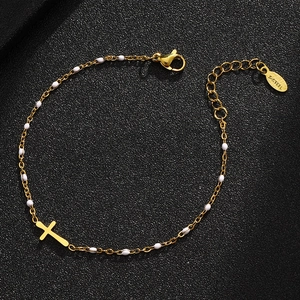 Detail of gold stainless steel cross bracelet with white beads and lobster clasp on black leather