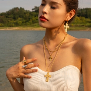 Double-layered gold cross necklace with vintage relief rings and earrings on model