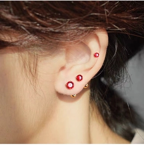 Close-up of red zircon stud earrings and golden ball ear studs worn in multiple piercings