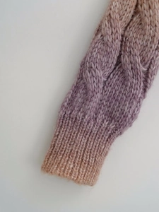 Detailed close-up of chunky knit sweater cuff with gradient camel to lilac cable pattern