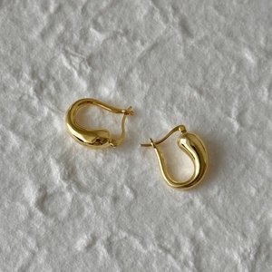 Detailed close-up of polished gold teardrop earrings on a white textured background