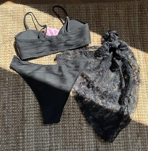 Flat lay detail of a black three-piece bikini set with ribbed texture and floral lace sarong