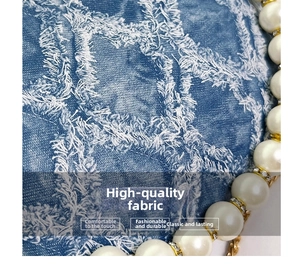 Macro shot of blue denim textured fabric with pearl chain and gold hardware details