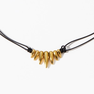 Gold stainless steel spike pendant necklace with black cord on white background