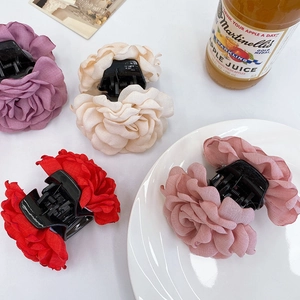 Flat lay of four colorful fabric rose hair claws in burgundy, champagne, pink, and purple