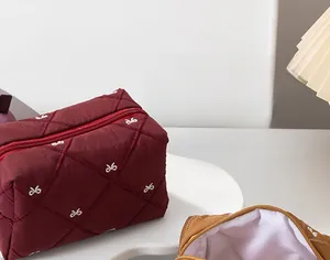 Close-up of wine red quilted cosmetic bag with white bow embroidery and diamond stitching