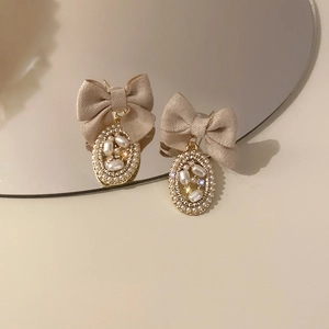 Detail of vintage bow earrings with beige fabric ribbon and pearl encrusted gold pendant