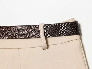 Détail d'une ceinture marron en similicuir serpent sur un pantalon en sergé beige