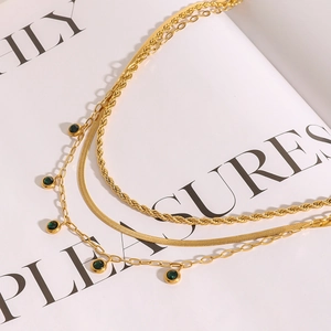 Detail of gold multilayer layered necklace with green gemstone pendants on white magazine