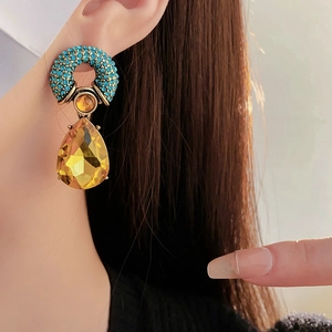 Dettaglio macro di orecchini vintage con cristallo ambra e anello di strass blu
