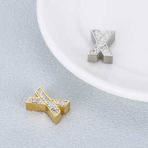Golden and silver stainless steel X letter pendants with crystals on a white plate