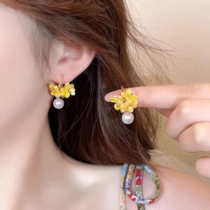 Détail de boucles d'oreilles fleur en résine jaune avec perle blanche sur mannequin