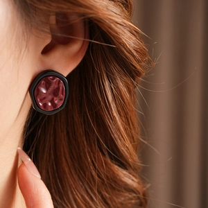Close-up of geometric irregular earrings with deep red textured center and black border