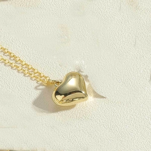 Macro shot of polished 3D heart pendant and fine gold chain necklace on stone texture