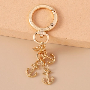Golden alloy keychain with anchor charms and a spring buckle on a beige background