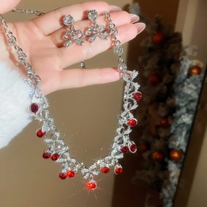 Detail of silver bow earrings and red gemstone necklace with festive Christmas tree backdrop