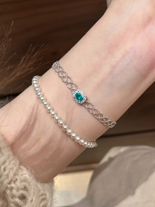 Close-up of stacked silver chain with green zircon stone and elegant pearl bracelet
