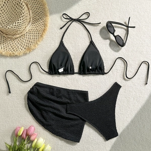 Detailed flat lay of black three-piece bikini set with ripple texture and beach accessories