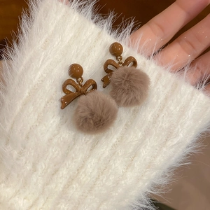 Dettaglio di orecchini a fiocco con pompon di peluche marrone chiaro su sfondo morbido