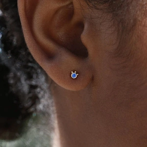Close-up of a gold-plated cat-eye stud earring with a blue gemstone on a model's ear