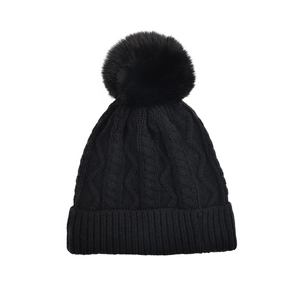 Close-up of black cable-knit winter hat with a large matching faux fur pom-pom detail