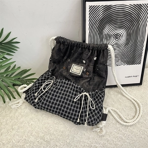 Detail of drawstring backpack featuring denim patchwork and black and white plaid pattern