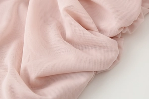 Macro detail of soft pink mesh fabric showing pleated texture and breathable net structure