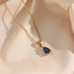 Détail du pendentif goutte en or 18 carats avec zircon bleu sur soie beige élégante