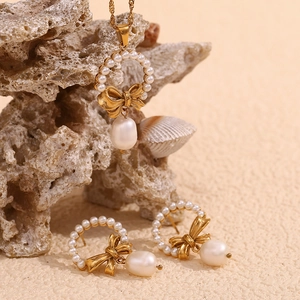 Detail view of 18K gold butterfly pearl necklace and earrings on beige textured stones