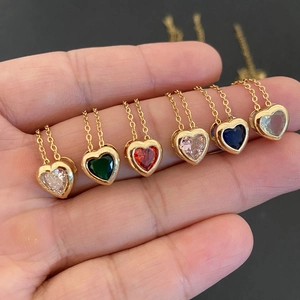 Detailed view of six gold heart necklaces with multi-colored gemstones held in a hand