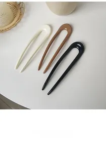 Close-up of three U-shaped hair pins in cream, amber, and black on a white table