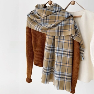 Detail of soft plaid scarf featuring camel and light blue pattern with fringed edges
