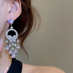 Gros plan de boucles d'oreilles argentées avec papillon en cristal et pendentifs gouttes