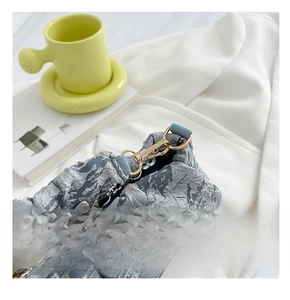 Detail of golden spring clasp and silver floral chain on blue pleated cloud bag