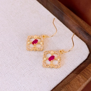 Detailed macro view of gold flower earrings with red ruby stone and white zircon
