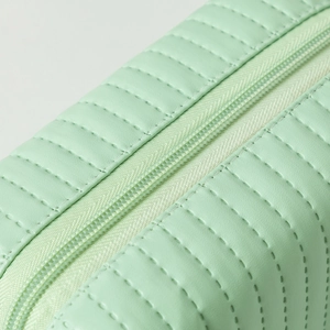 Close-up of mint green travel cosmetic bag with quilted texture and smooth zipper detail