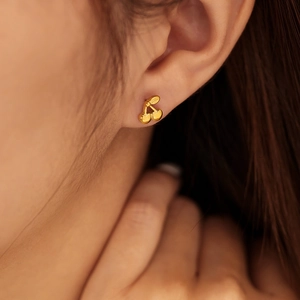 Close-up of a delicate gold cherry stud earring worn on the earlobe with metallic finish