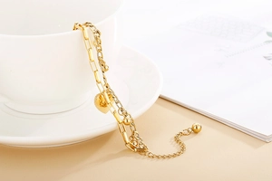 Golden double-layer chain bracelet with heart pendant on white ceramic cup edge