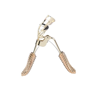Professional golden eyelash curler with black non-slip grip handles on white background