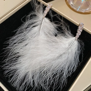 Macro shot of white feather earrings with diamond accents in a luxury black gift box