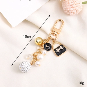 Golden keychain with pearl beads, number 5 charm, and black bow bag pendant on beige cloth