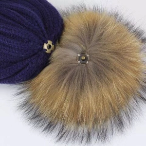 Close-up of metal snap button connecting a fur pompom to a purple chunky knit beanie