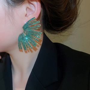 Macro detail of geometric fan earrings featuring green rhinestones and gold-tone plating