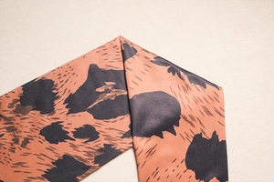 Close-up of silky leopard print fabric showing smooth satin texture and elegant brown pattern