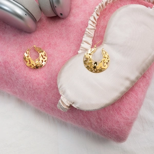 Détail de boucles d'oreilles vintage en dentelle dorée sur un pull en maille rose