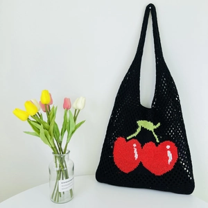 Detail of black knitted mesh tote bag featuring iconic red cherry pattern and woven texture
