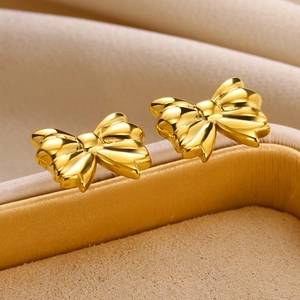 Macro shot of elegant golden bow stud earrings displayed on a beige jewelry box edge