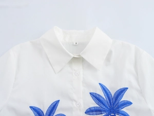 Detailed close-up of blue leaf embroidery on white resort-style button-up shirt collar